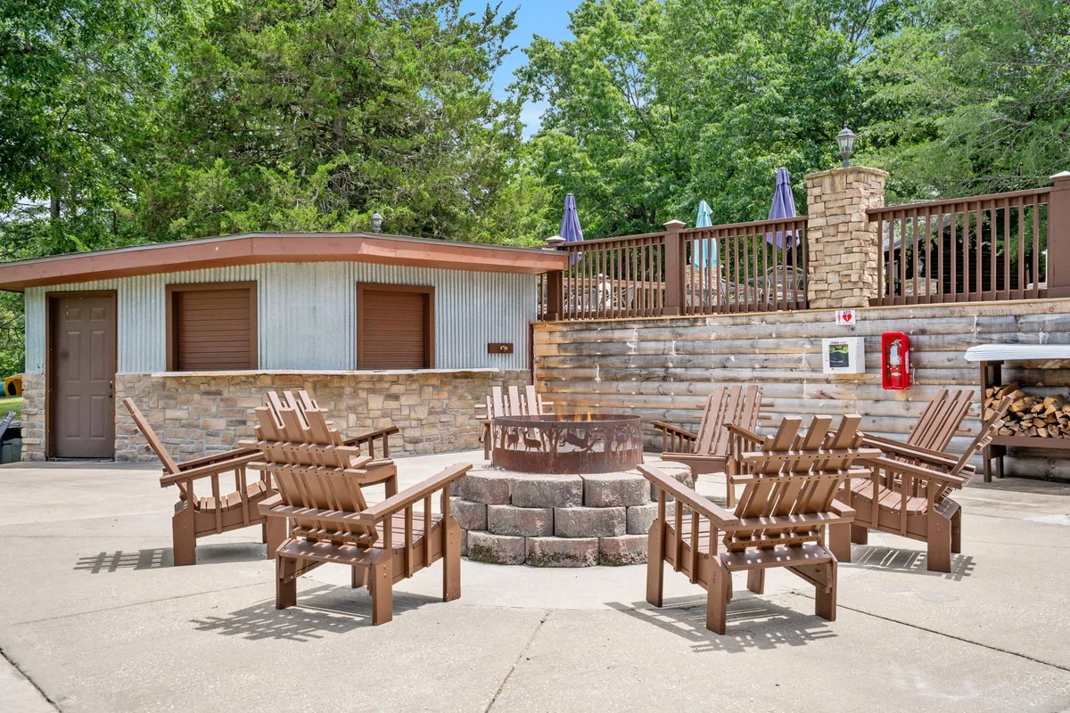 A cozy outdoor fire pit area featuring Adirondack chairs, a wooden deck, and a rustic stone wall. The setup encourages gatherings around the fire for storytelling, celebrations, or relaxing under the stars, surrounded by nature.