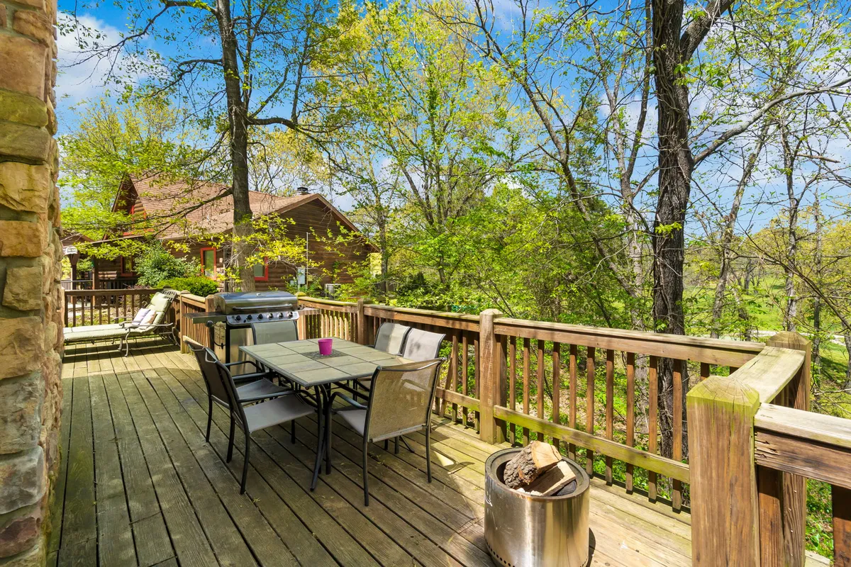 An outdoor dining area with a wooden table and grill, complemented by a fire pit and enveloped by tall trees. The mood is intimate and tranquil, perfect for cozy dinners, relaxed evenings, or moonlit gatherings under the stars.