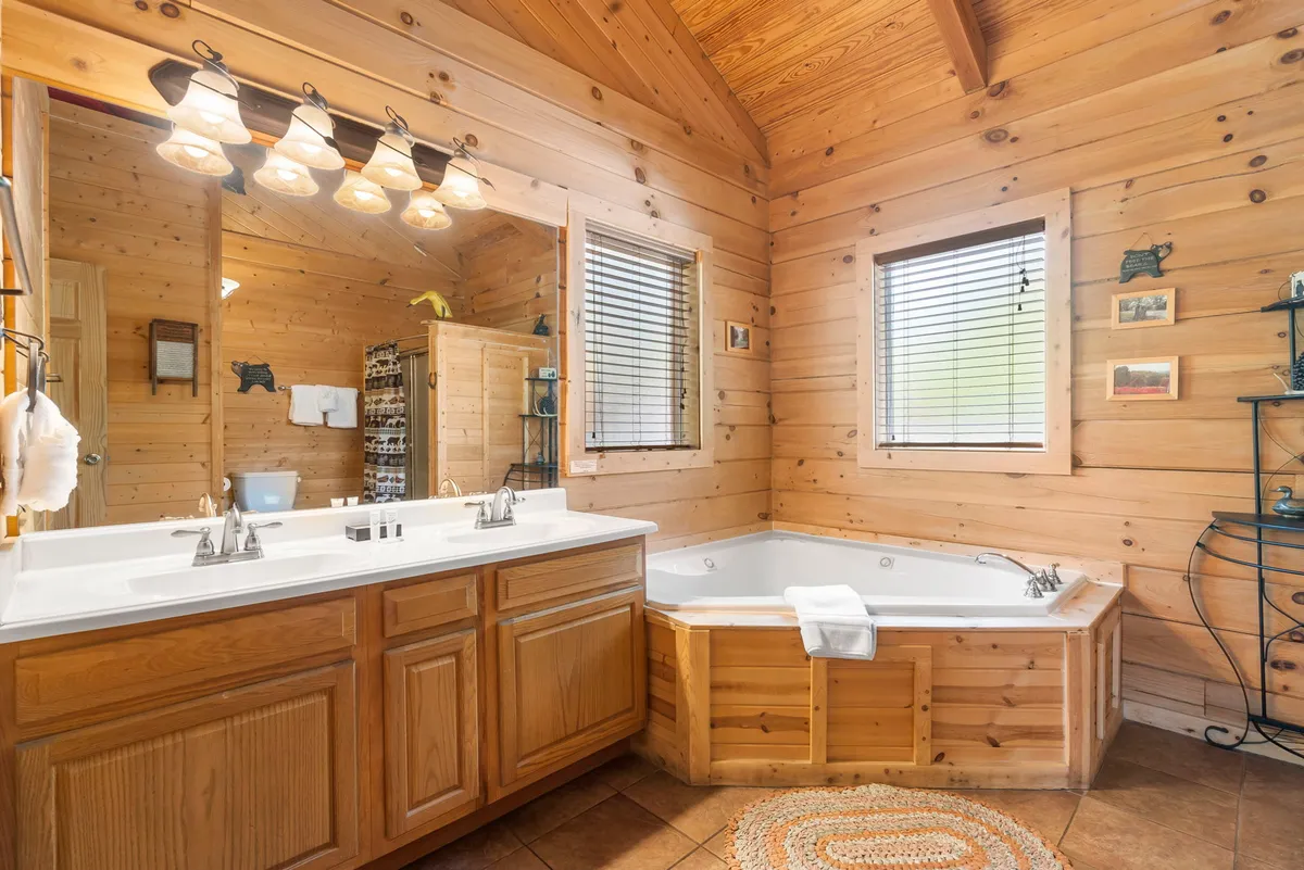 A warm, wood-paneled ensuite bathroom featuring a luxurious jetted jacuzzi tub and a double sink vanity, offering plenty of space for two. Natural light filters through, enhancing the spa-like atmosphere.