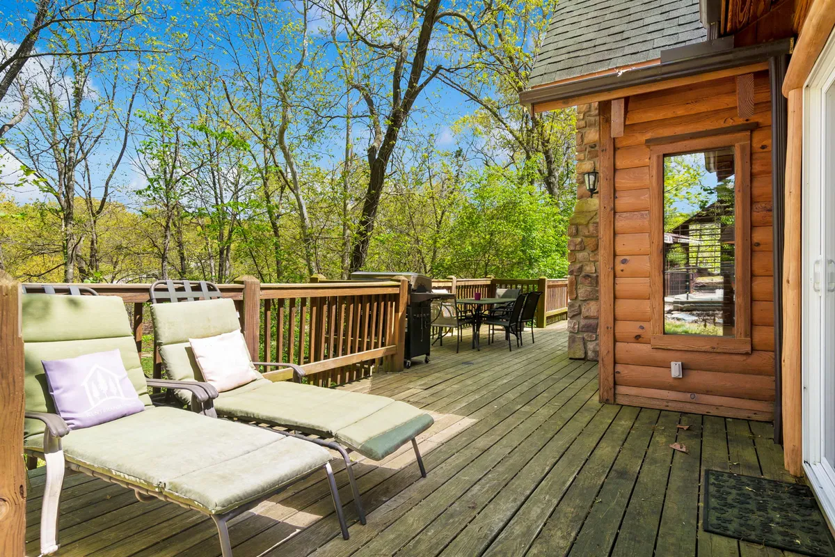 This serene exterior shot features a large wooden deck surrounded by greenery, with two lounge chairs and a dining table set for an outdoor meal. The peaceful setting invites relaxation, sunbathing, or alfresco dining, all while immersed in nature.