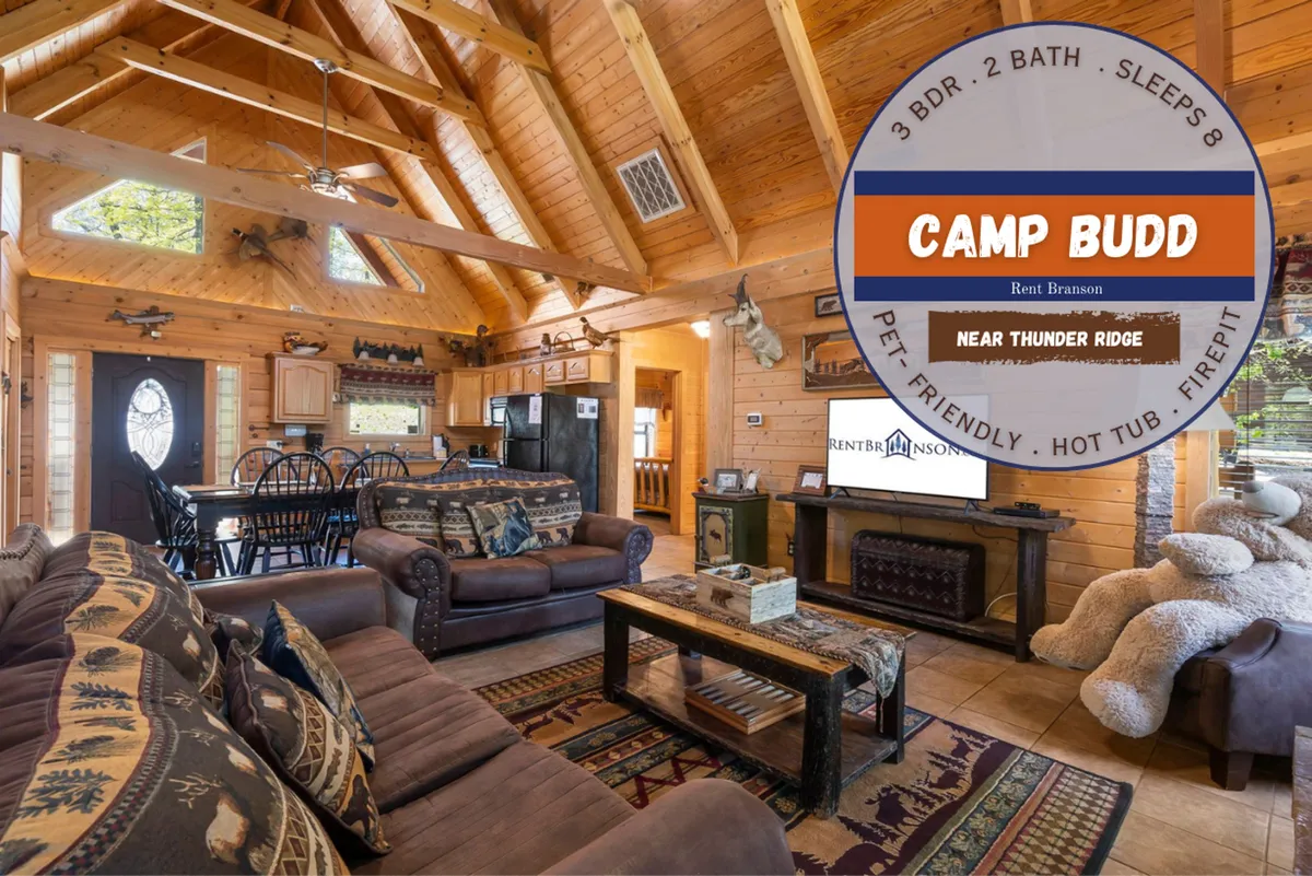 A wide view of the living area that shows comfortable seating grouped around a fireplace, exposed wooden beams stretching overhead, large windows revealing the surrounding woodland, and a glimpse of the adjacent dining area. The scene radiates warmth and encourages communal activities like movie nights or game sessions.